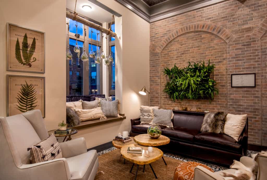The lobby of a popular boutique hotel in Boston is seen with exposed brick walls, couches, tall windows, and warm lighting