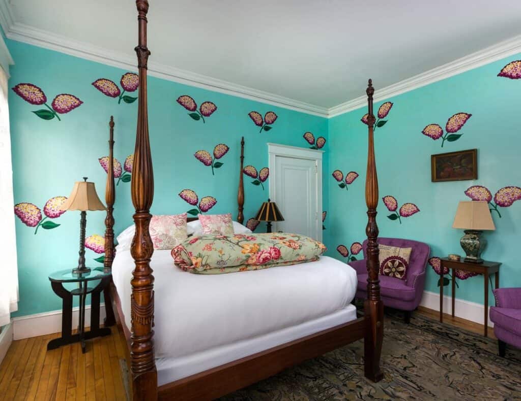 A four poster bed sits in the middle of a room with flowers painted on teal blue walls in a beautiful boutique hotel in Portland, Maine
