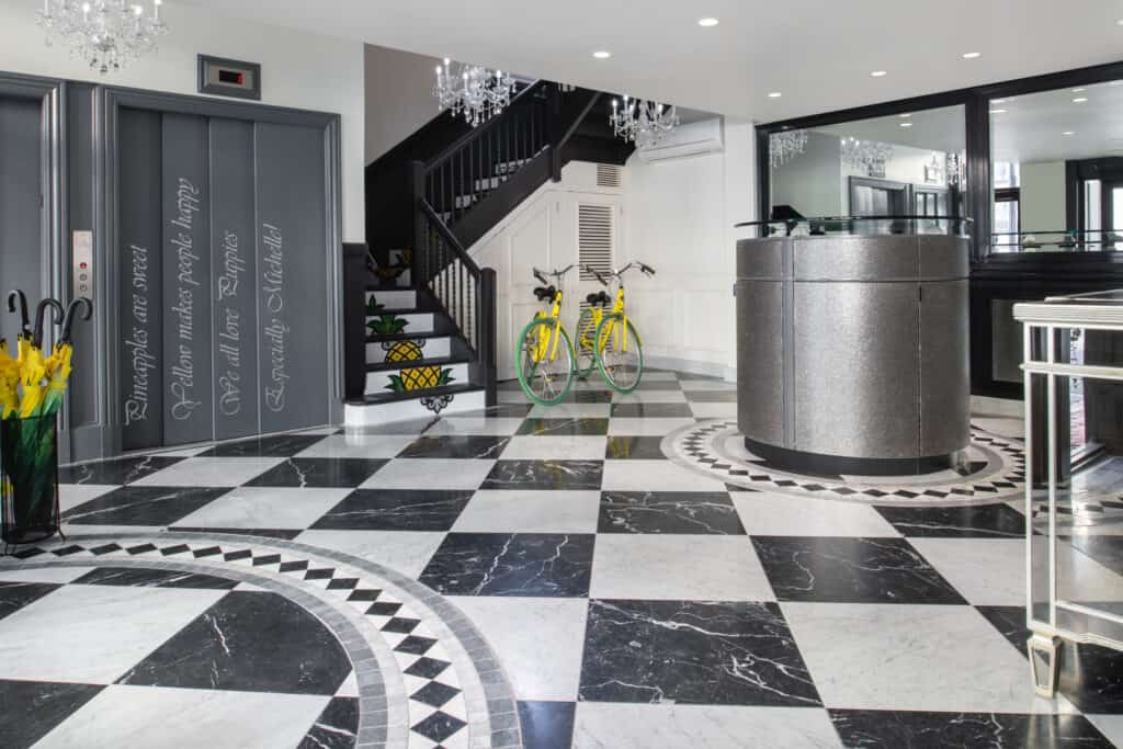 The lobby of a Boston boutique hotel is seen with black and white checkered floor, elegant chandeliers, and yellow pops of color