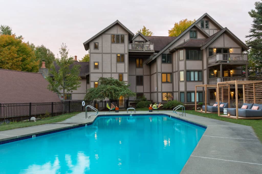 an inviting lodge-style hotel sots behind a large and empty swimming pool, dusk time