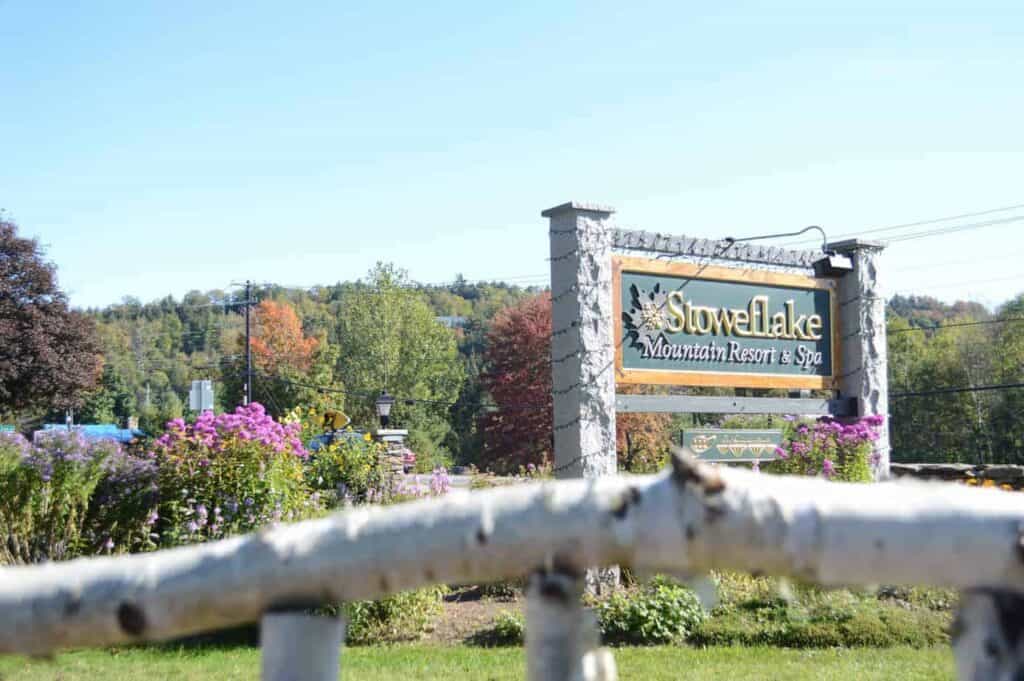 image of a hotel sign seen from a slight distance, sign reads stoweflake resort, in the background are autumn-tinged trees
