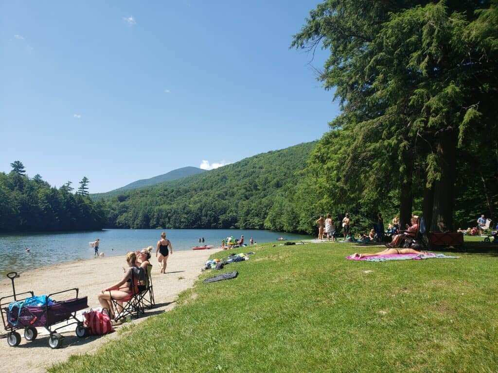 people relaxing on a beach near a grassy hill on a sunny summer's day by a lake in Vermont