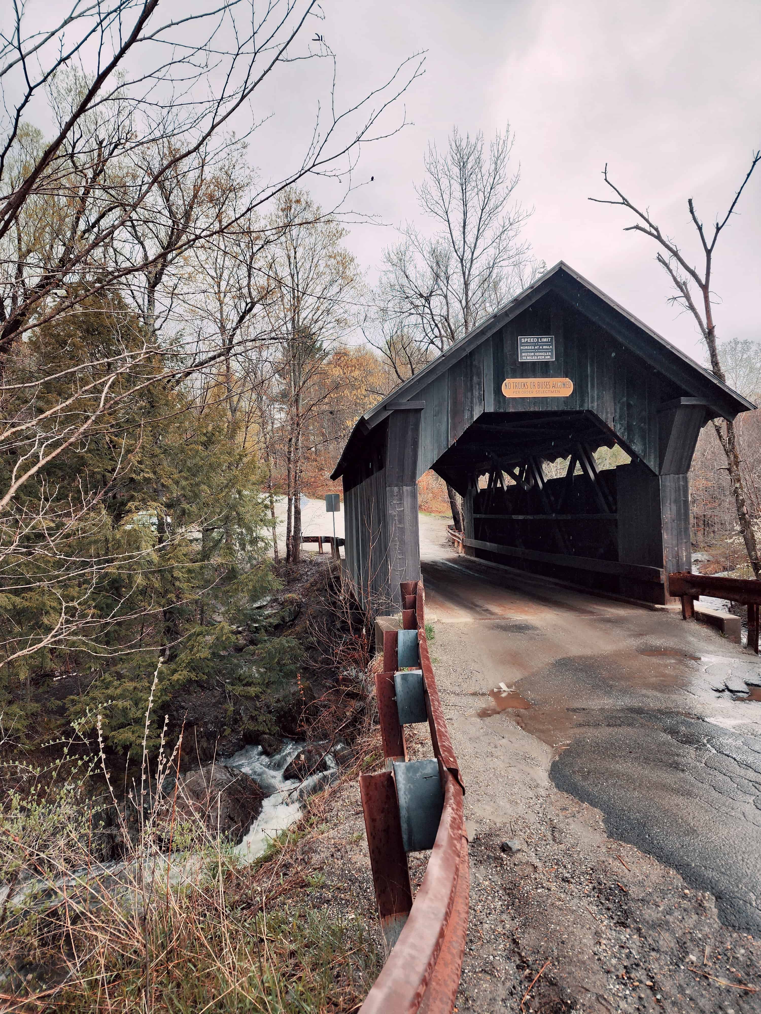 a gloomy day shows a muddy road leading to a dark brown covered bridge in Vermont