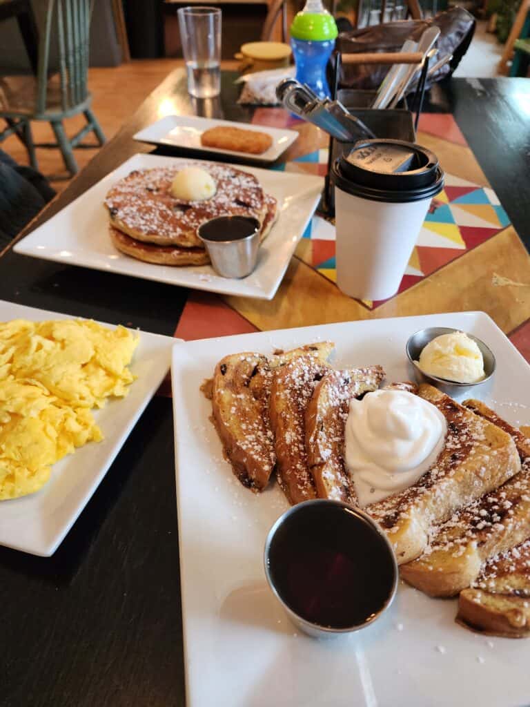 a big breakfast spread, french toast, pancakes, scrambled eggs, coffee, on a colorful table