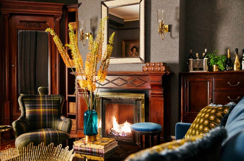 A moody lobby with a dramatic mirror as a focal point above a mantel with a roaring fireplace is seen at one of the top bed and breakfasts in Newport, Rhode Island