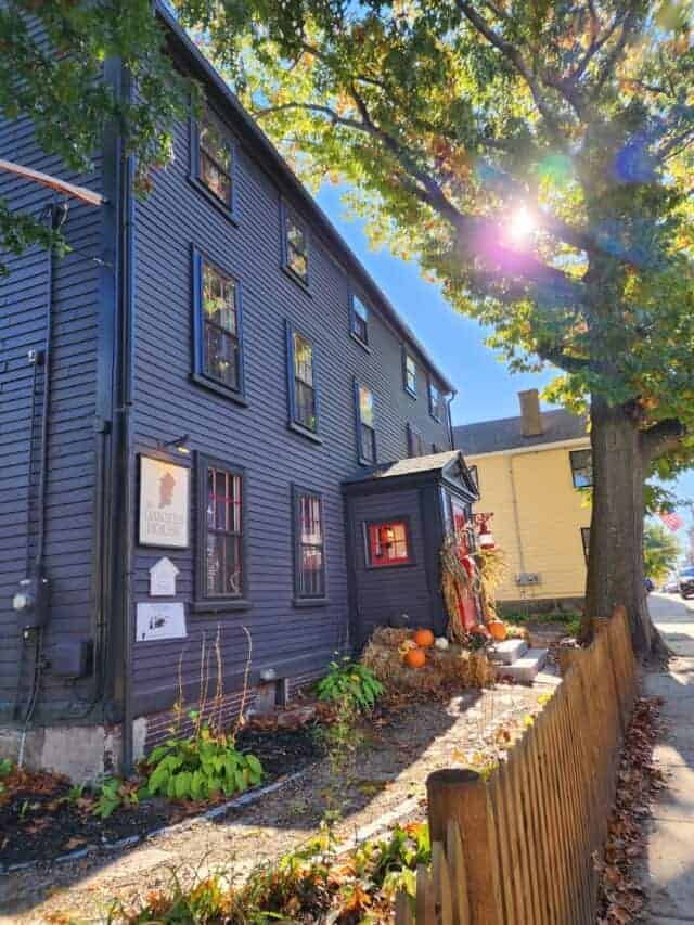 A large deep blue historic haunted bed and breakfast in Salem, Massachusetts during fall with autumn decorations like pumpkins and hay bales around the front door.