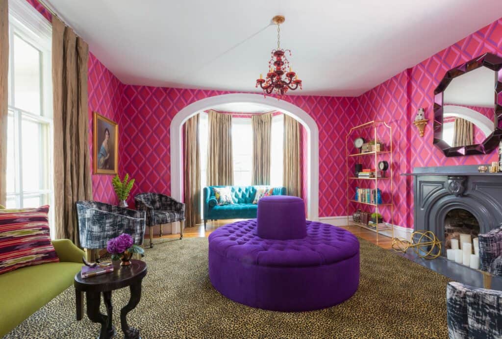 A dramatic sitting room with purple furniture, deep pink walls, and a black fireplace is seen