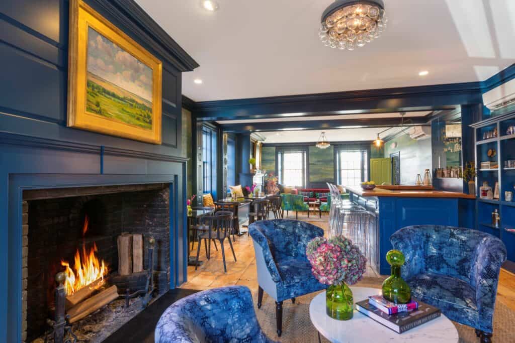 A historic Salem MA that is said to be haunted is seen with deep blue walls, eclectic furnishings, and a roaring fireplace.