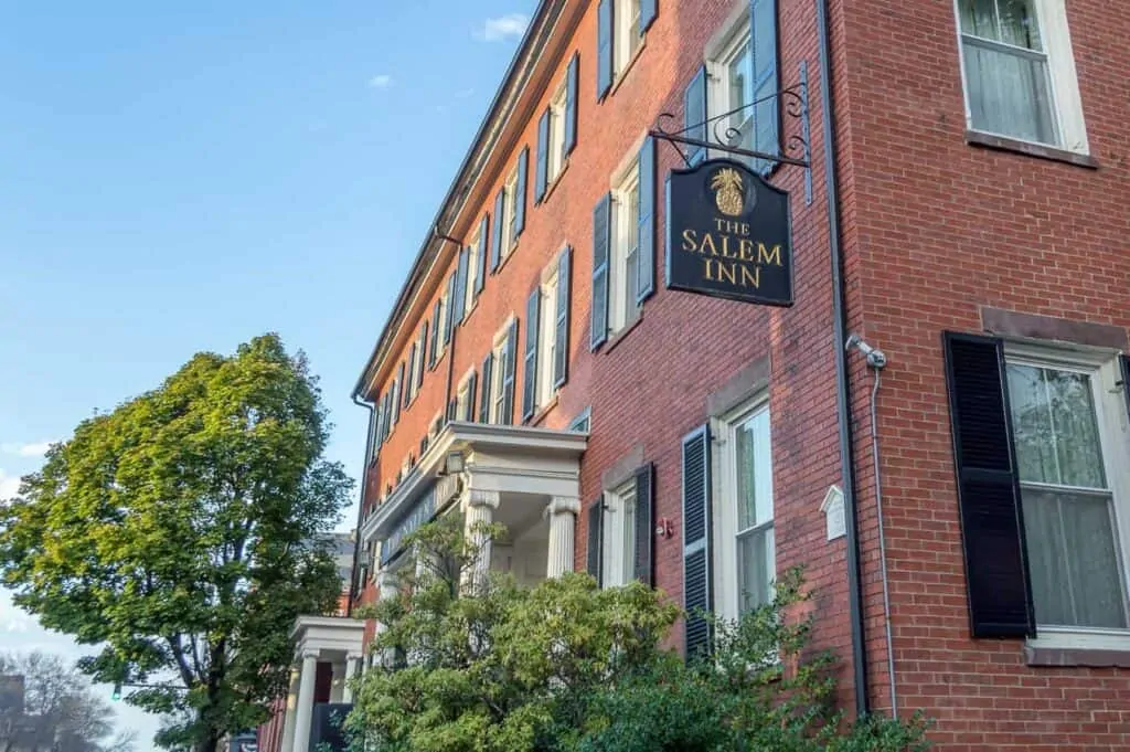 A large brick historic inn in Salem, Massachusetts with green trees in front and blue skies overhead