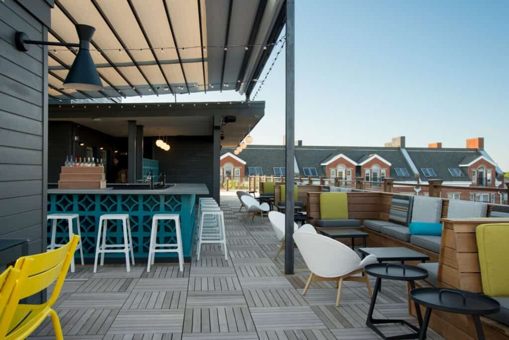 A rooftop bar with a teal and yellow color scheme has outdoor lighting and minimalist furnishings