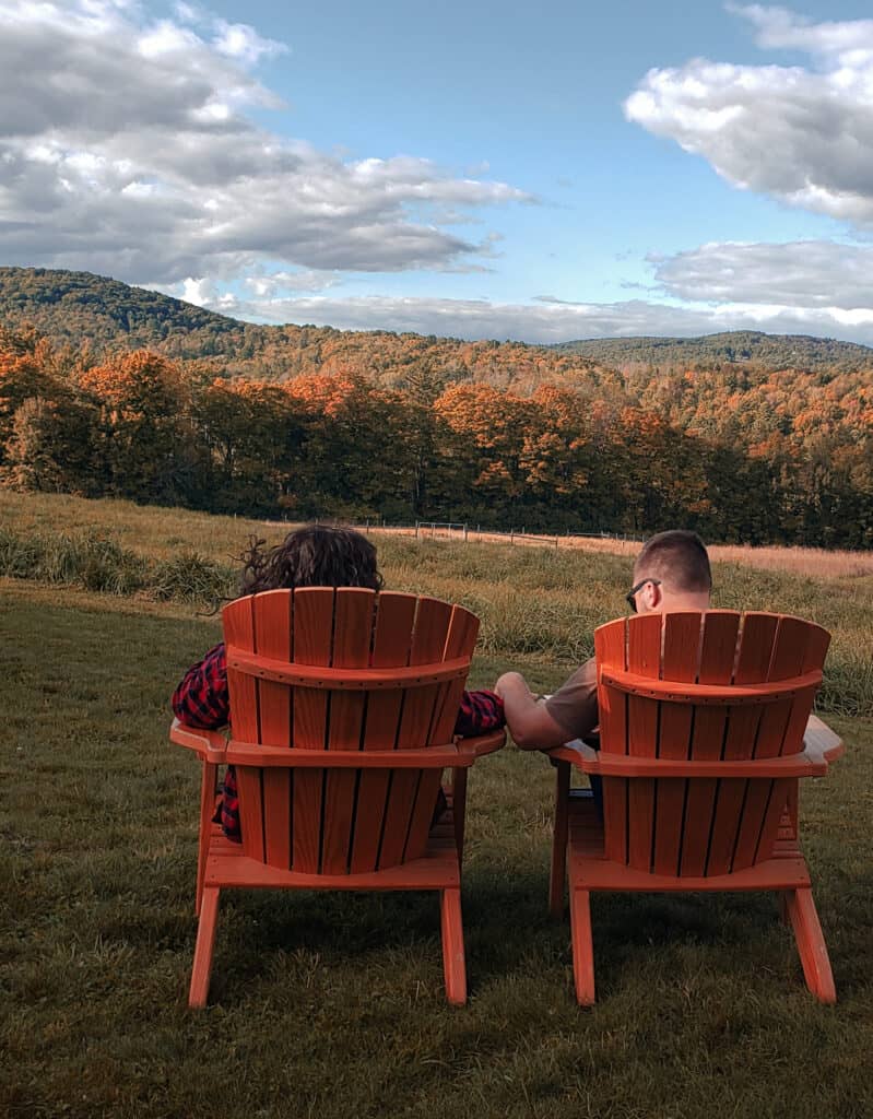 A couple sit in chairs and look out on Vermont fall foliage