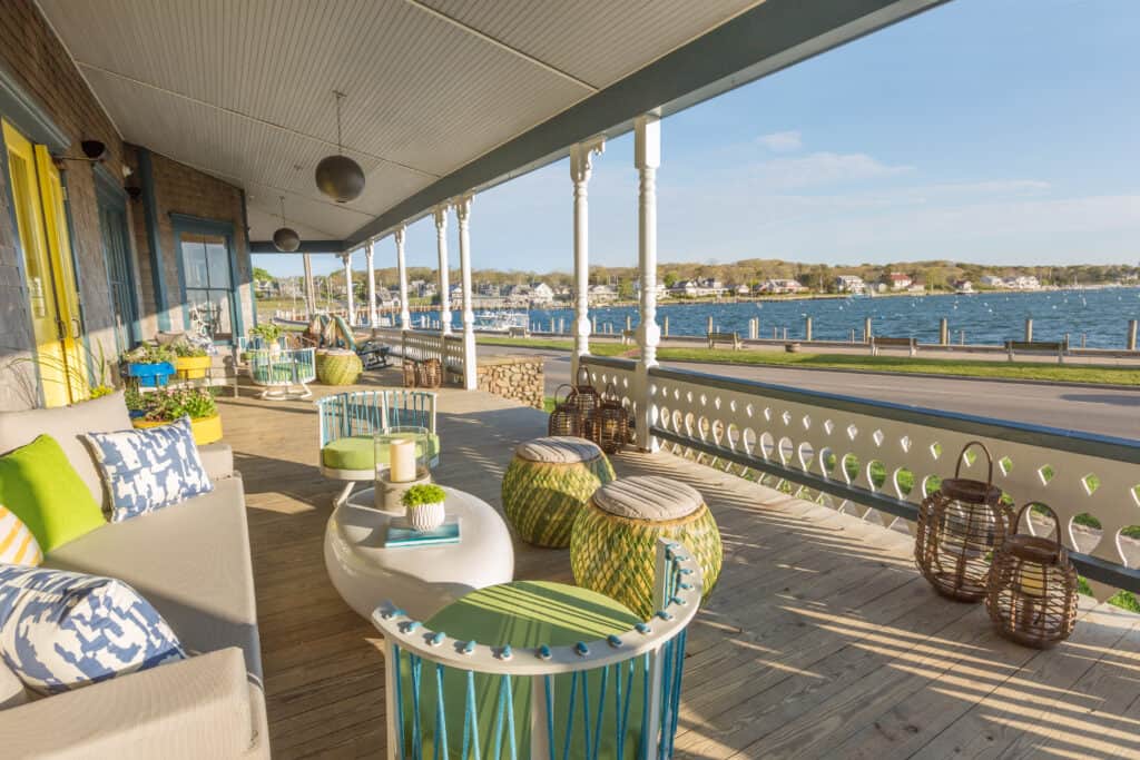 A spacious front porch decorated with coastal colors and outdoor furniture overlooks the waterfront