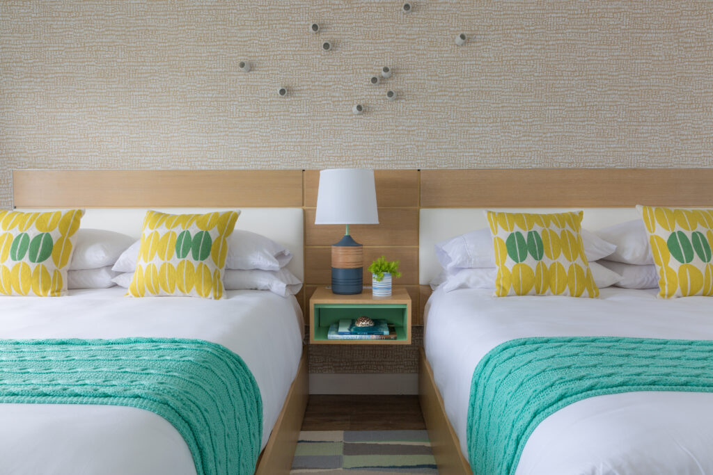 Double beds decorated in a coastal theme are separated by a small table and lamp in a Martha's Vineyard hotel room