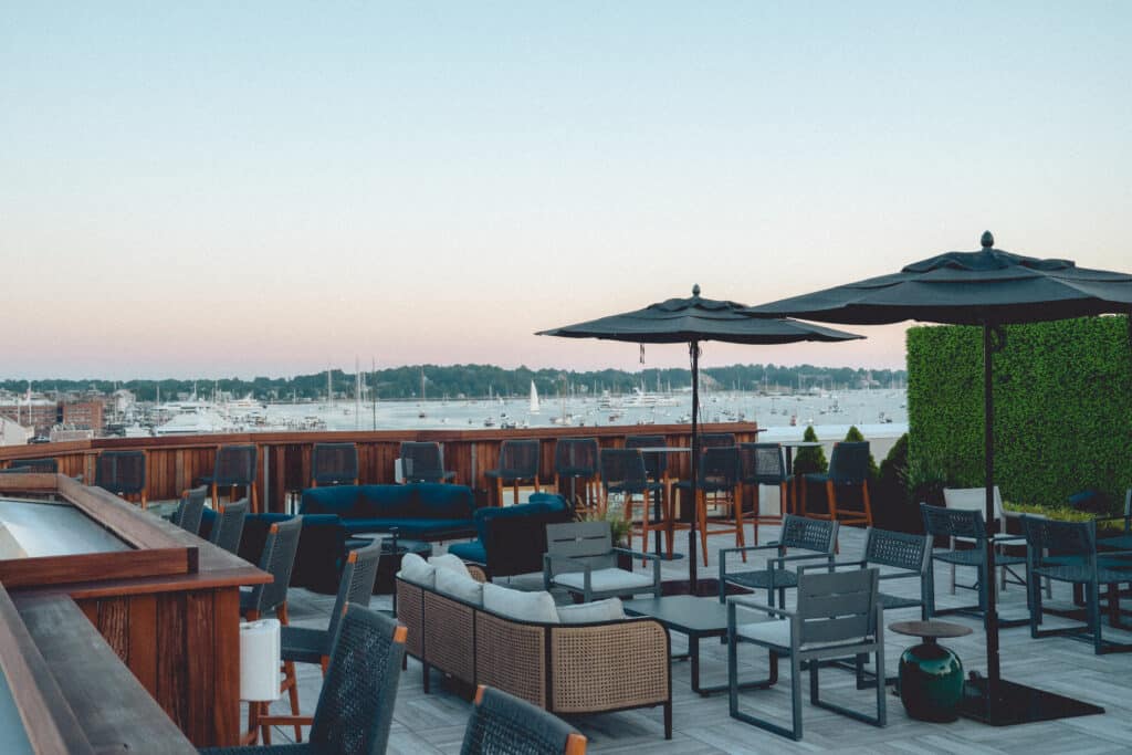 An outdoor rooftop at one of the top boutique hotels in Newport RI is furnished with tables and chairs and has beautiful waterfront views