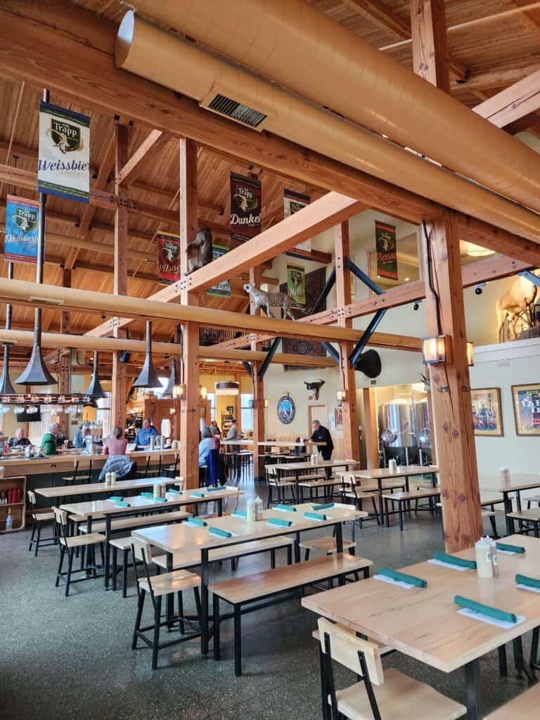 interior of a bright and clean beer hall with high ceilings and banners hanging from them. lots of long tables sit empty and ready for guests