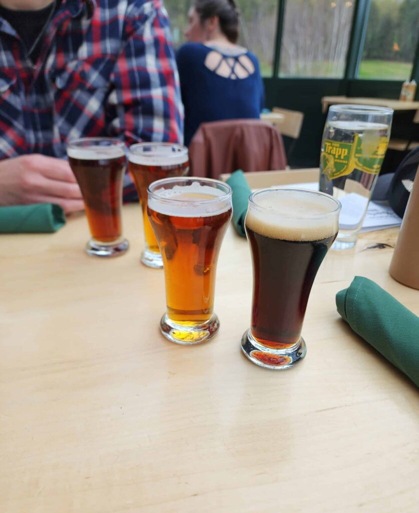 photo of 4 sample sized beers on a table. in the background a man's arm is seen, clad in flannel