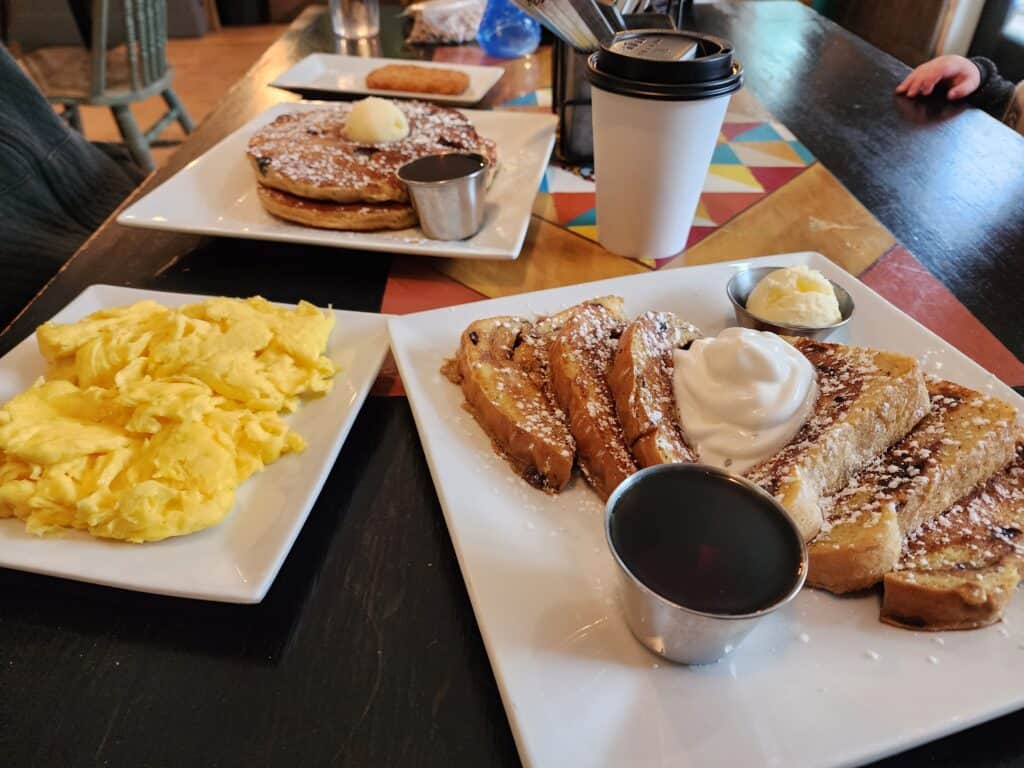 a delicious breakfast spread on a table, a few plates contain french toast scrambled eggs and pancakes