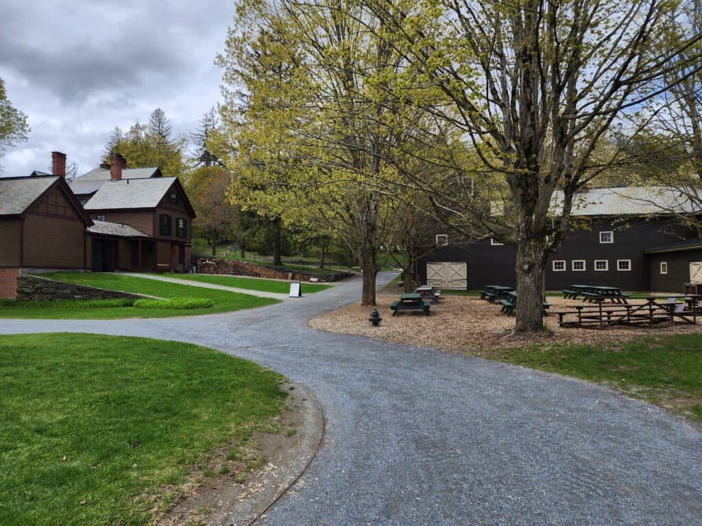 a gravel path connects several farm buildings and a historic house on a spring day in vermont. the trees are just starting to bloom