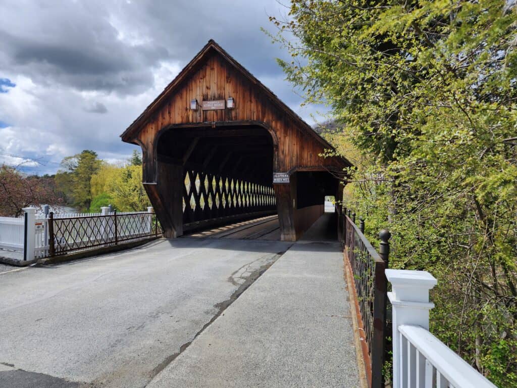 a dark brown covered bridge sits at the end of a short lane