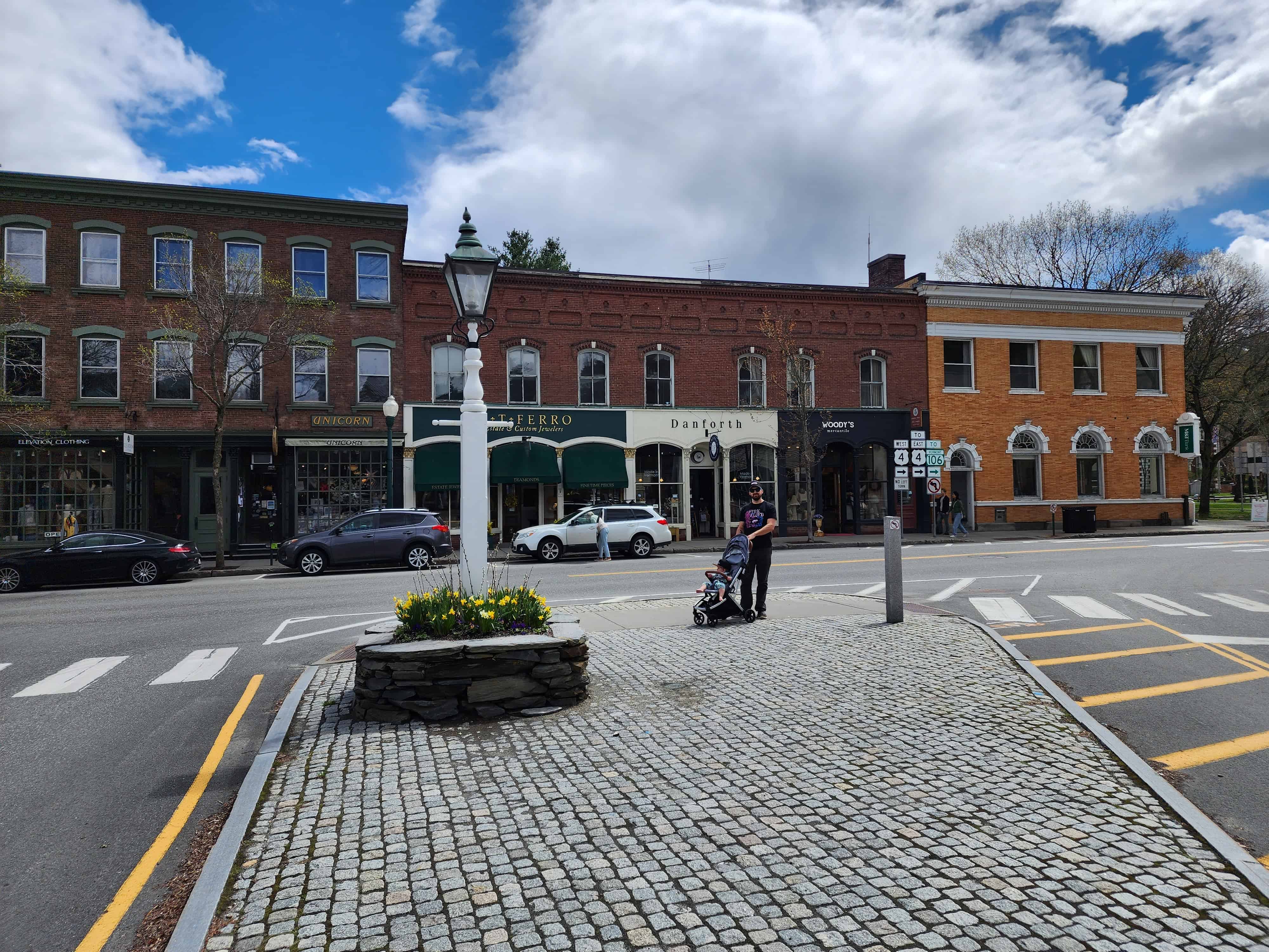 Woodstock Vermont town square with brick shops in the distance, a man pushing a stroller looks at the camera