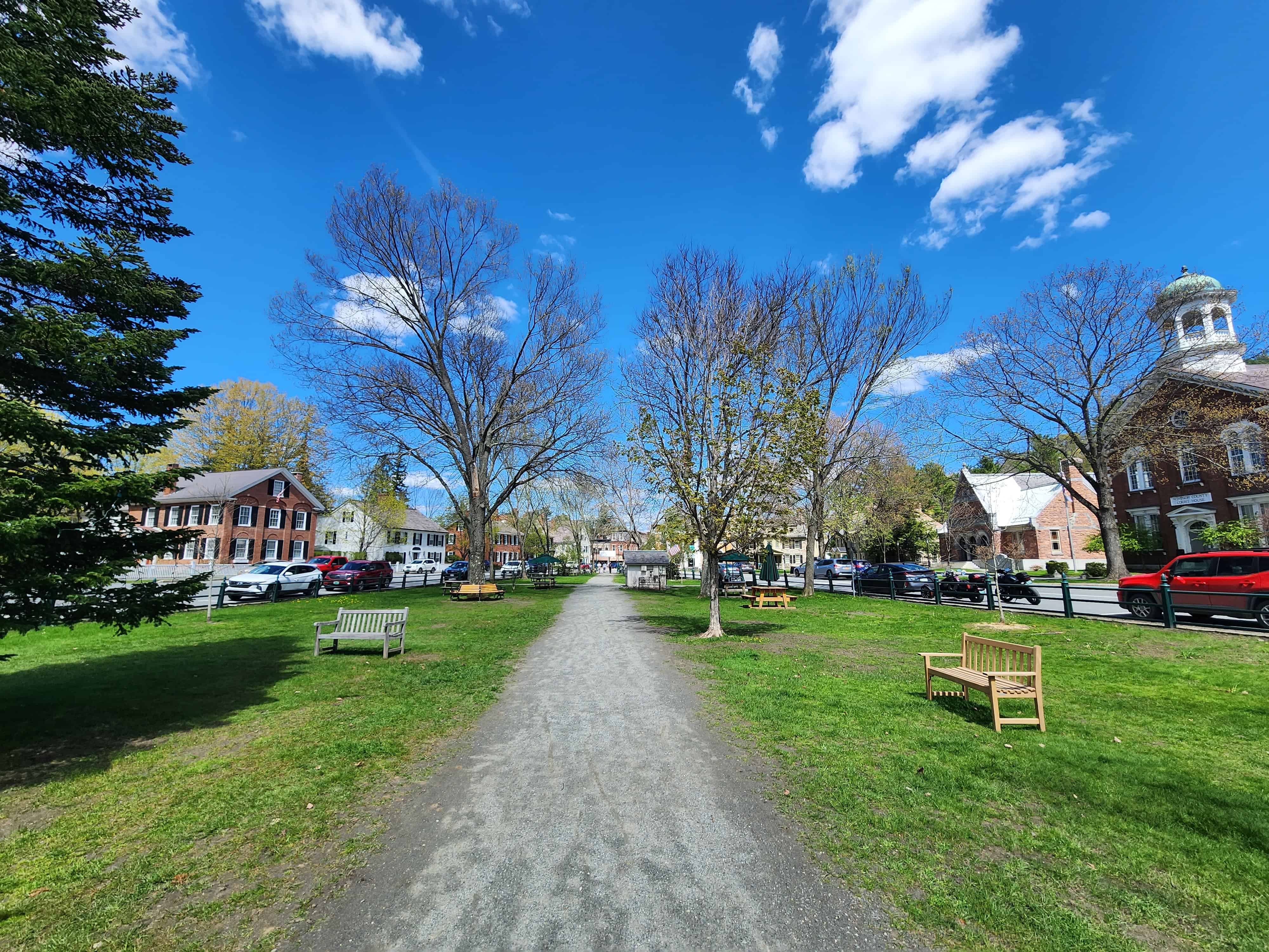 a rocky path runs through a village green in a charming Vermont town. the sky is blue, grass is green, and historic buildings line the roads