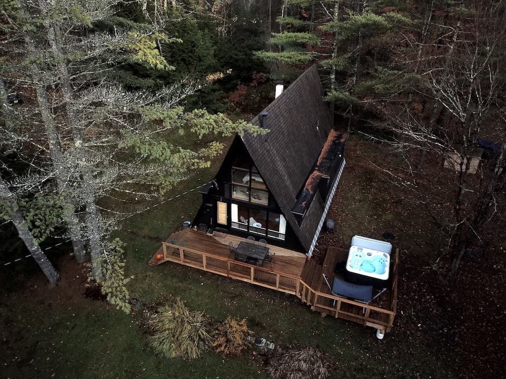 Aerial view of an a-frame in the woods with a jacuzzi.