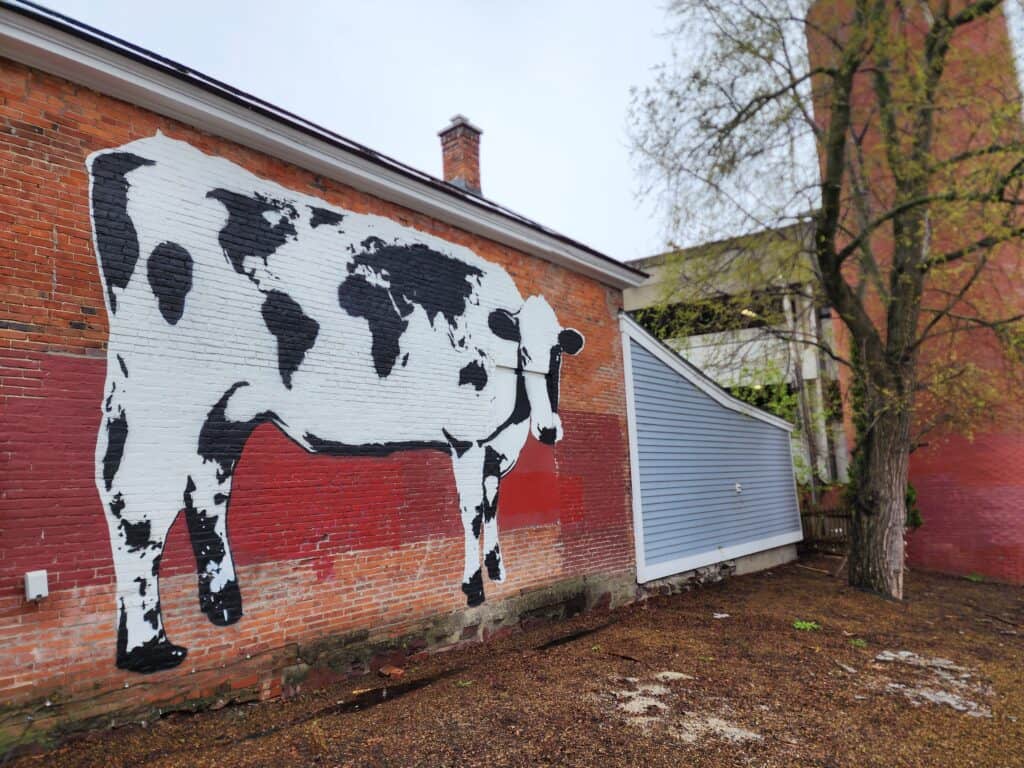 large wall mural of a cow. its spots are in the shape of a world map