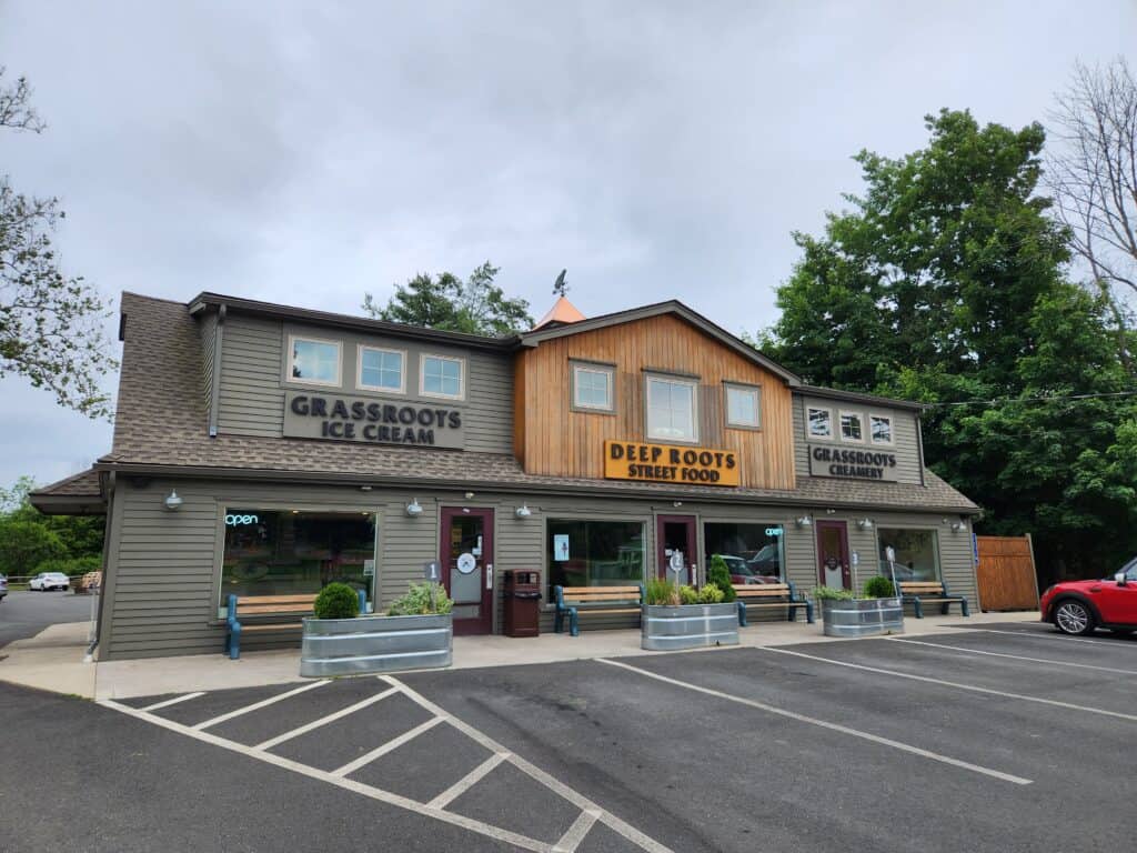 A building in a parking lot with three shops and metal planters in front under grey skies