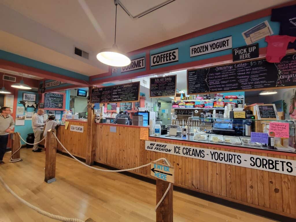 A long ice cream counter at a Connecticut ice cream shop with wooden floors and wooden paneling counter