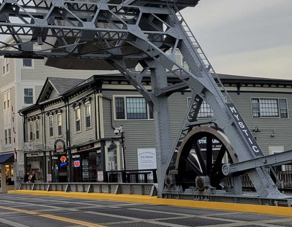 A large metal drawbridge in Mystic, Connecticut sits with shops beyond