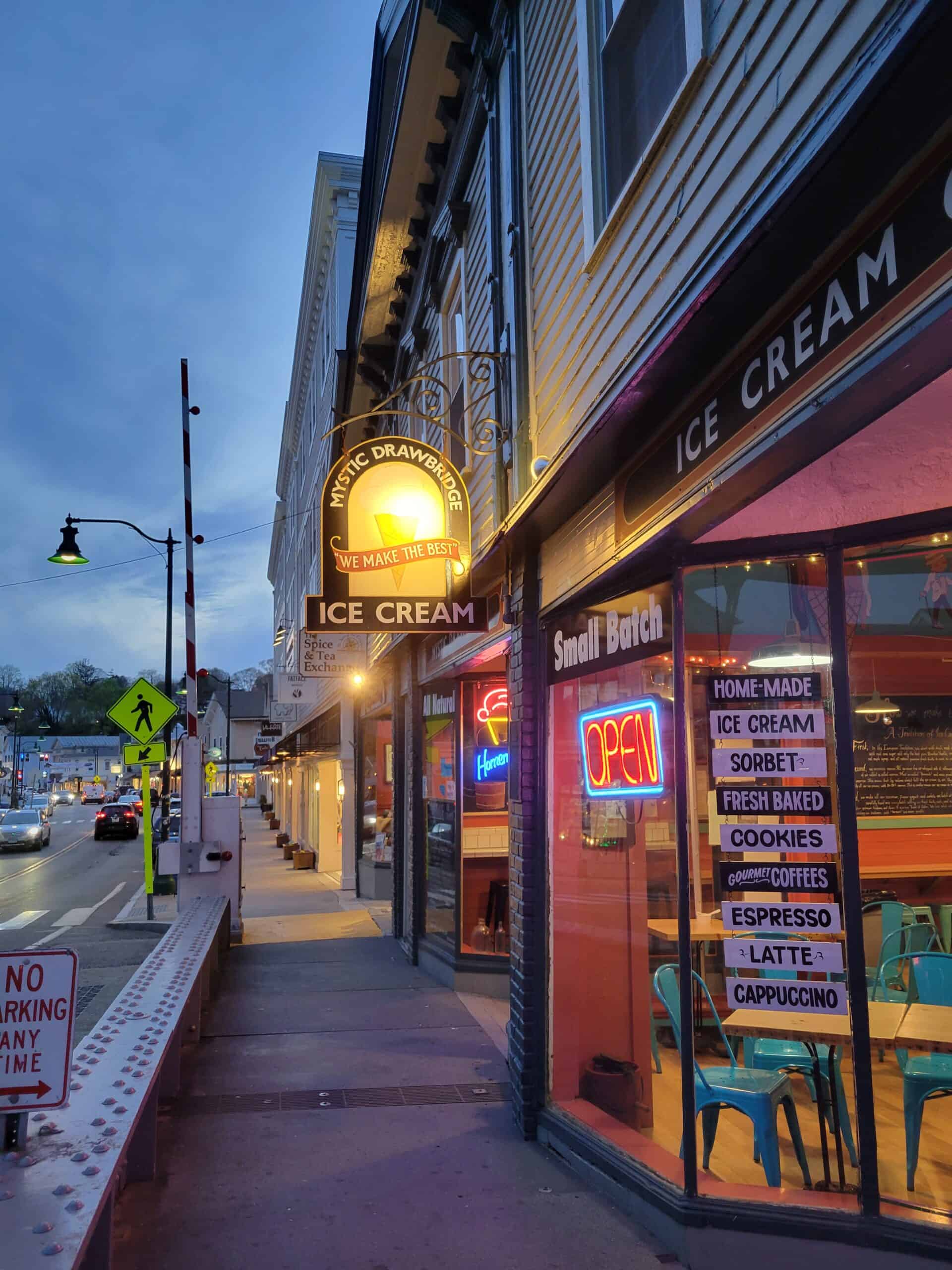 An ice cream shop sign in Mystic, Connecticut is on a narrow strip that includes several shops on one side and a busy roadway on the other