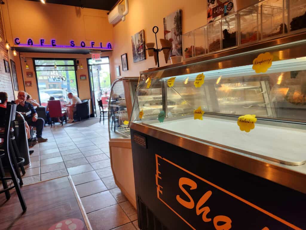 The interior of an ice cream shop cafe in Connecticut with a long counter, seating with customers, and a neon sign reading Cafe Sofia