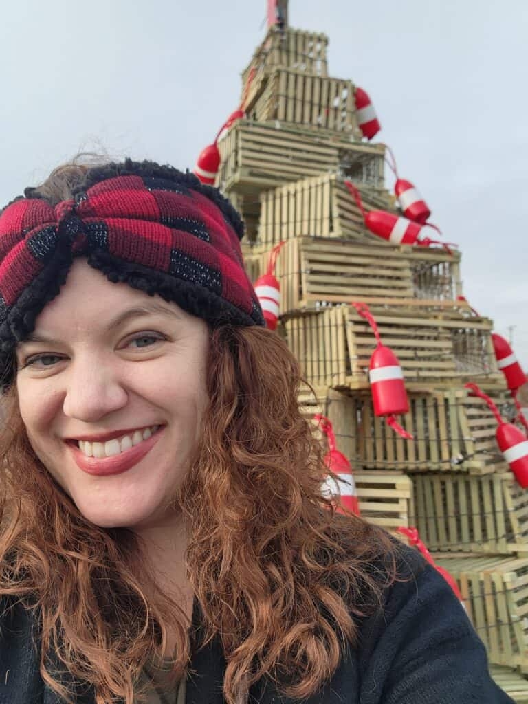 A woman poses smiling in front of a lobster trap tree in coastal Maine