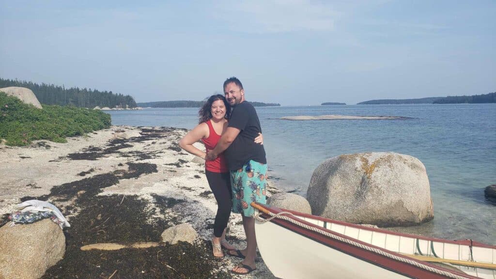 A man and a woman pose in a hug on a beach in Deer Isle Maine