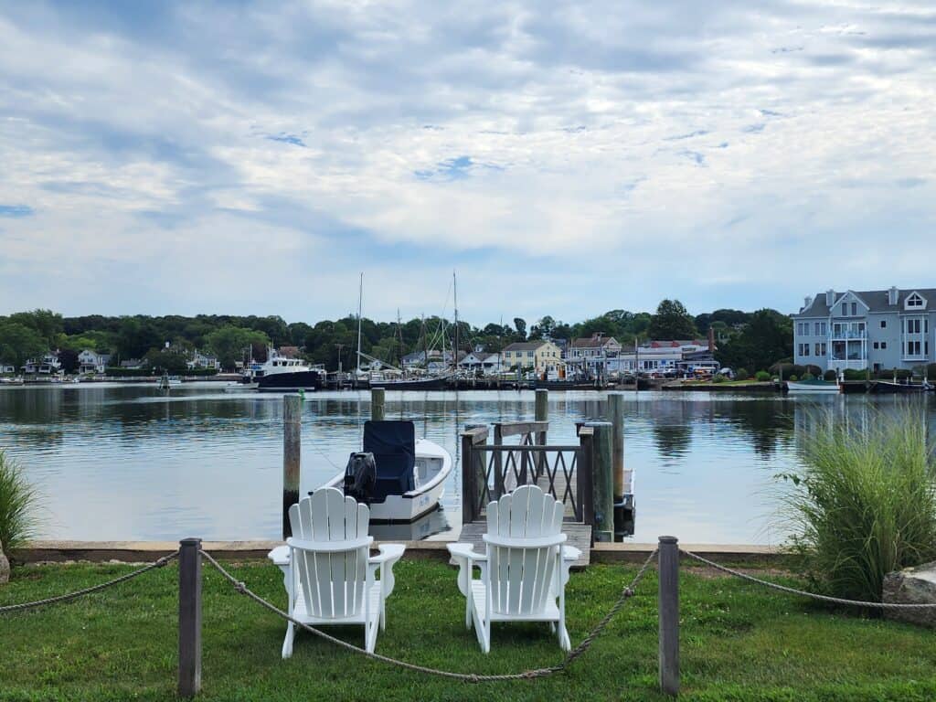 two white adirondack chairs face a calm river in mystic CT