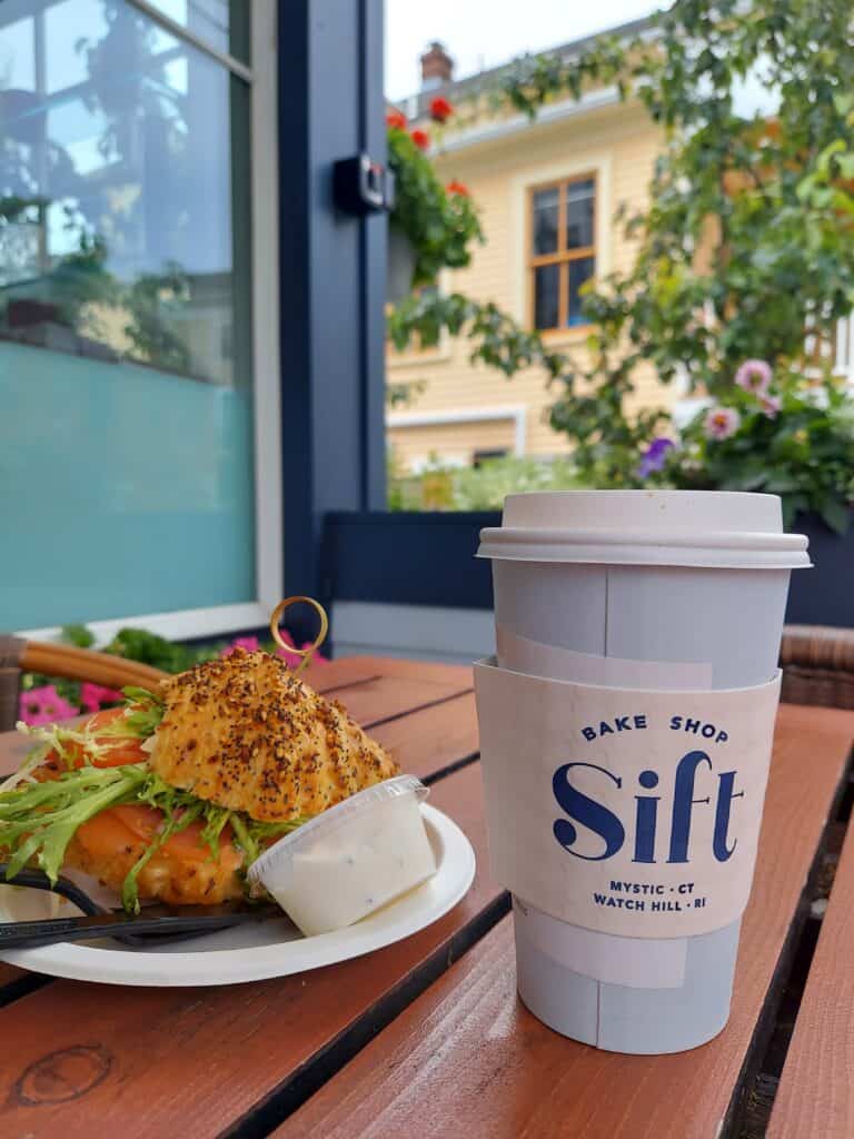 a table on a patio with a bagel and a coffee cup that says Sift bake shop