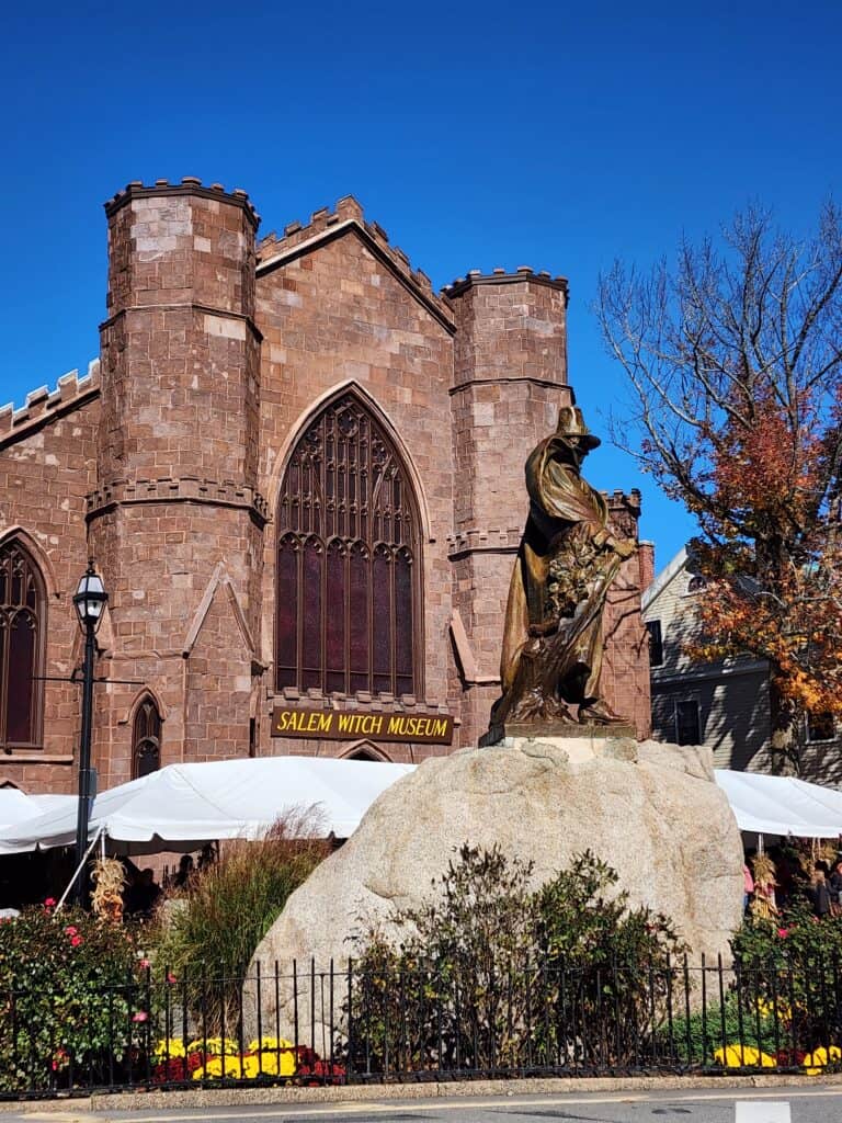 A large brick building with a statue of a witch on a large rock in front under a blue sky