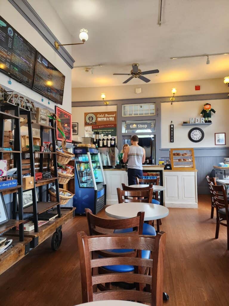 the cozy interior of a coffee shop and cafe with several bistro table and chairs and a man standing at a counter