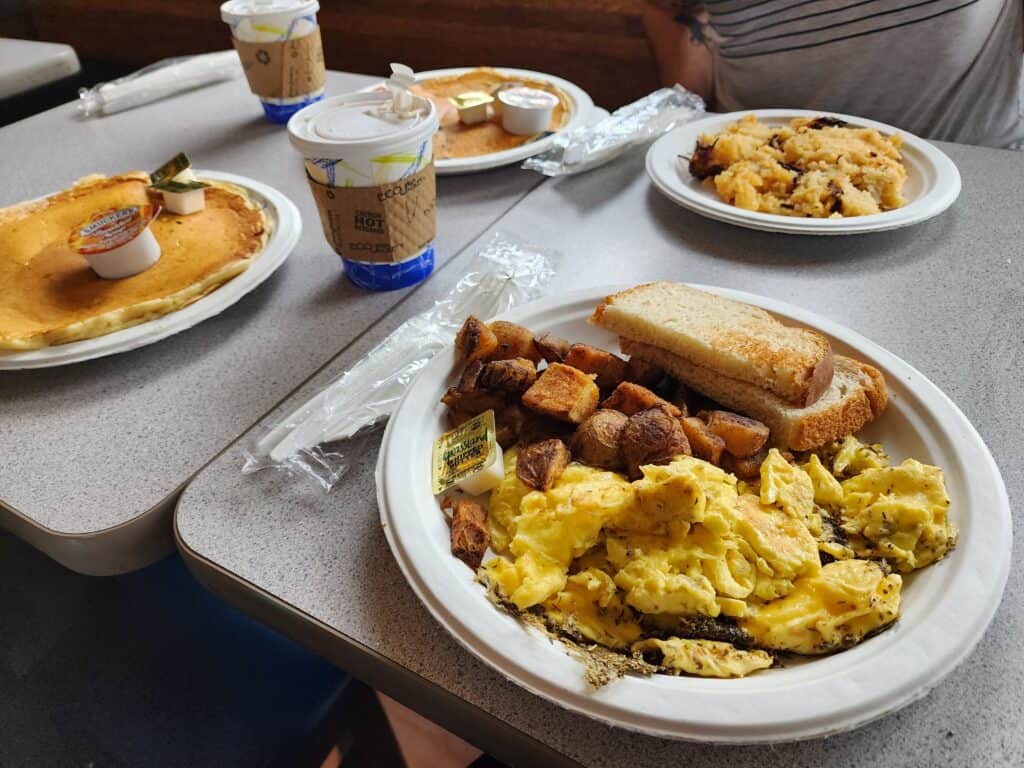 a full breakfast spread including eggs, toast, pancakes, and coffee set on paper plates and using paper cups