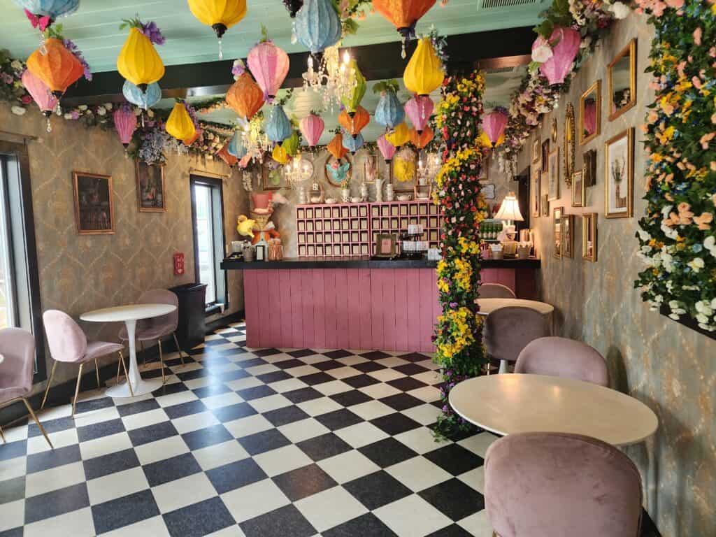 interior of an empty cafe that is whimsically decorated. there are flowers everywhere and colorful lamps hanging from the ceiling