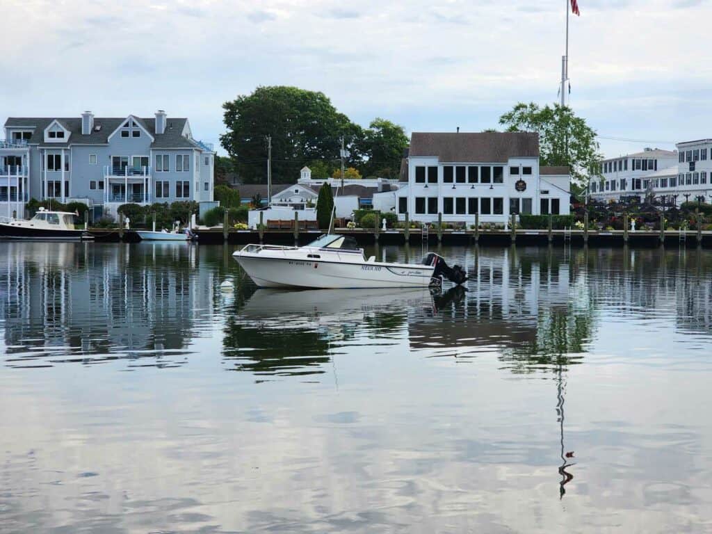 a motor boat sits quietly on the mystic river in CT with white shops and homes behind