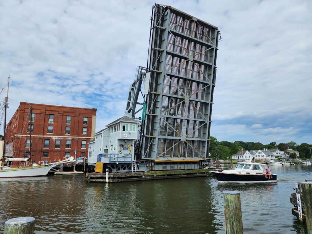 a metal drawbridge is raised over a river in Mystic, Connecticut as a small yacht passes beneath