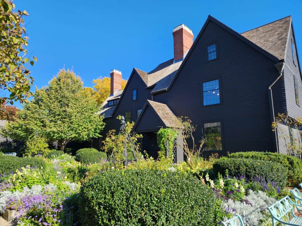 A large historic home that is known as the House of the Seven Gables is seen surrounded by greenery under a blue sky