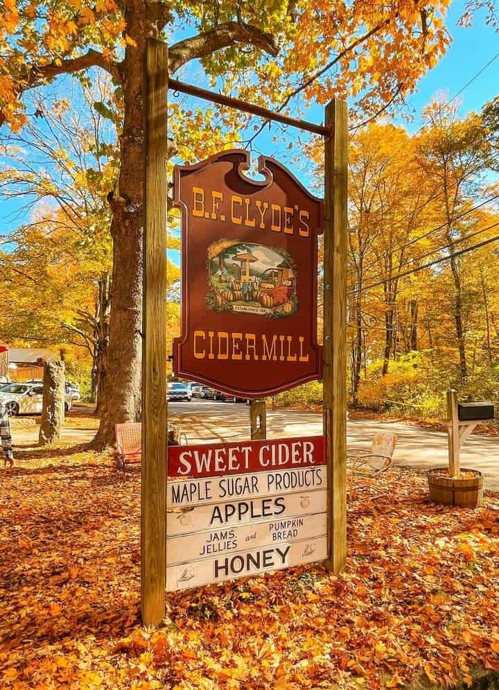 photo of a sign for BF Clyde's Cider Mill in Connecticut, advertisiting sweet cider, maple sugar products, apples, etc. fall leaves all around