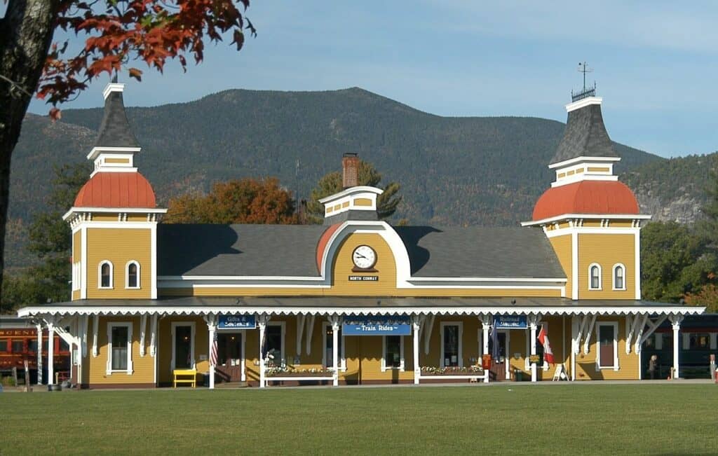 a yellow, vintage style train station in new hampshire with a mountain behind