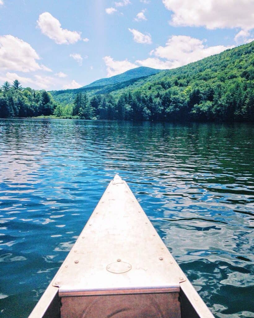the front of a canoe in a beautiful emerald lake manchester vt, mountains in the distance