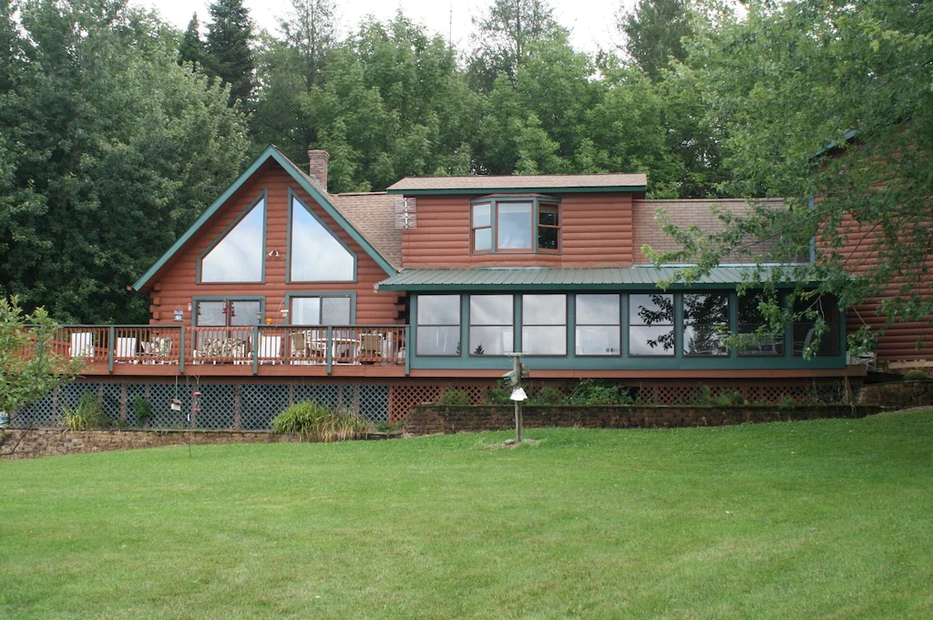 A spacious Vermont cabin with many windows sits with woods behind it