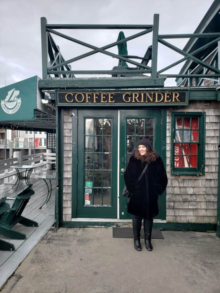 amy standing in a black fur coat in front of a shop with a sign that says Coffee Grinder