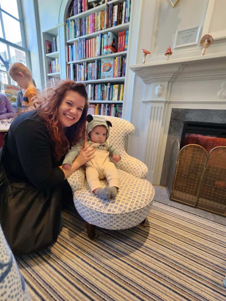 amy, a women in her 30's, squatting next to a young baby propped up in a chair. they are in a bookstore
