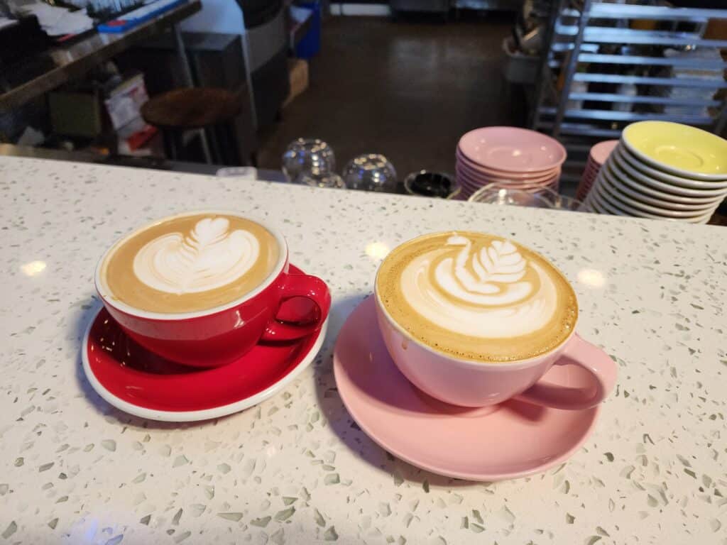 two lattes sit on a counter in red and pink mugs, beautiful latte art on top